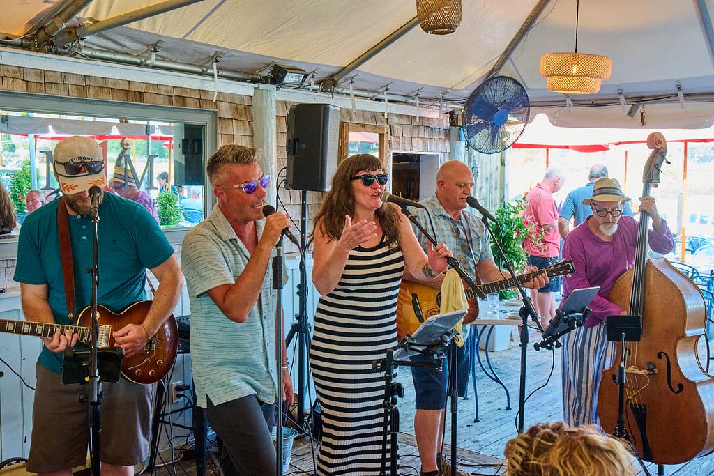 Three people singing on a deck and one playing guitar