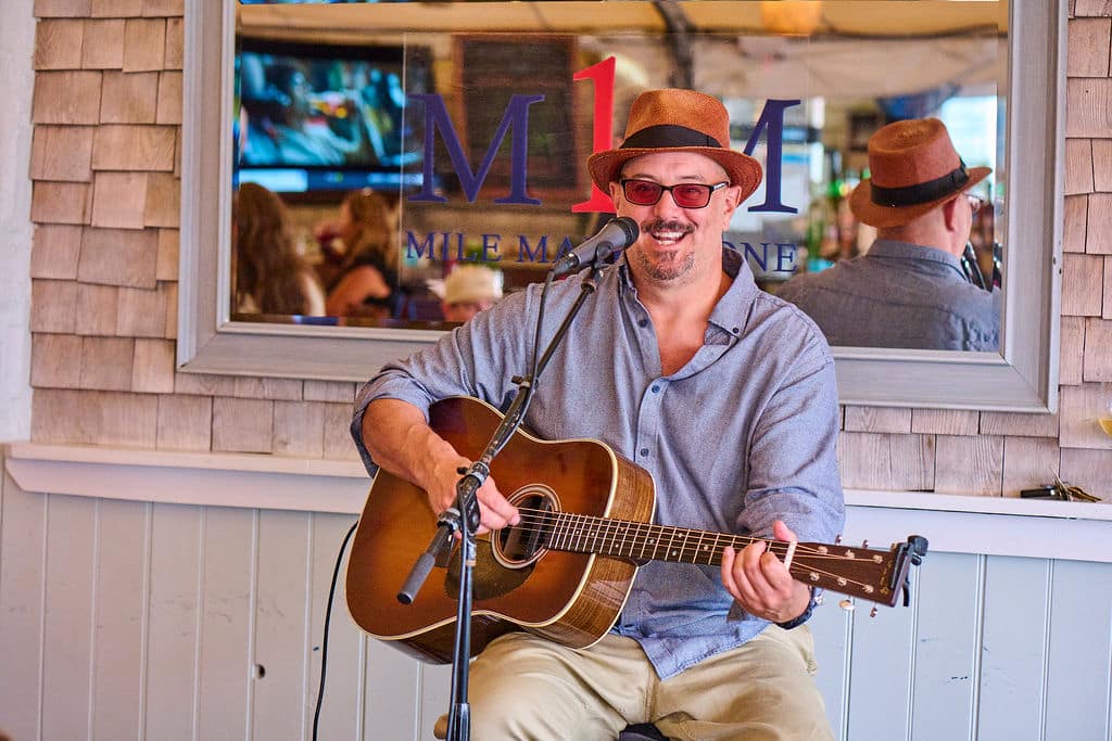 man with mustache hat playing guitar sitting on a stool
