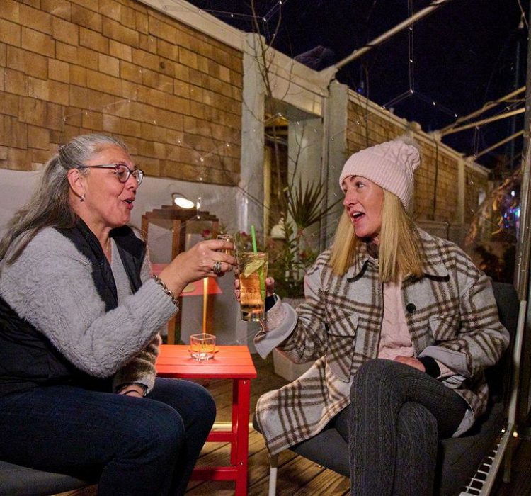 Two women cheers in winter clothes in a clear dome