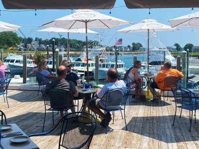 dining on a deck with boats in the background under white umbrellas on a sunny day