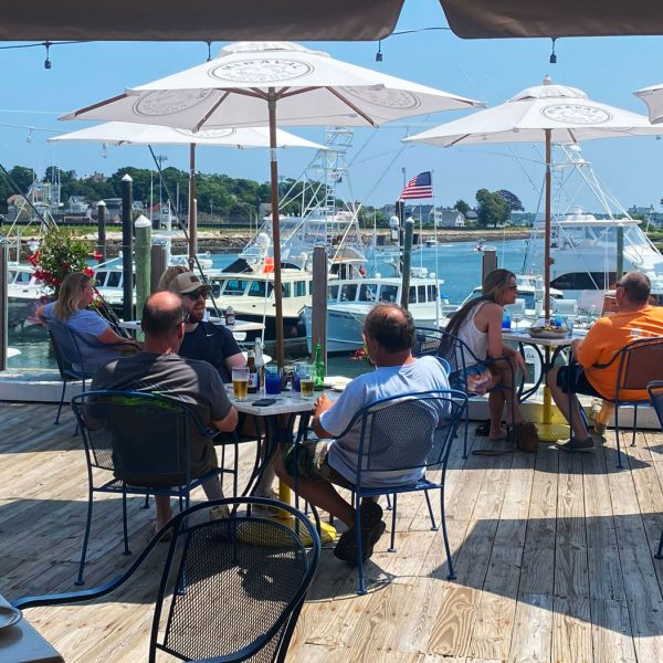 dining on a deck with boats in the background under white umbrellas on a sunny day