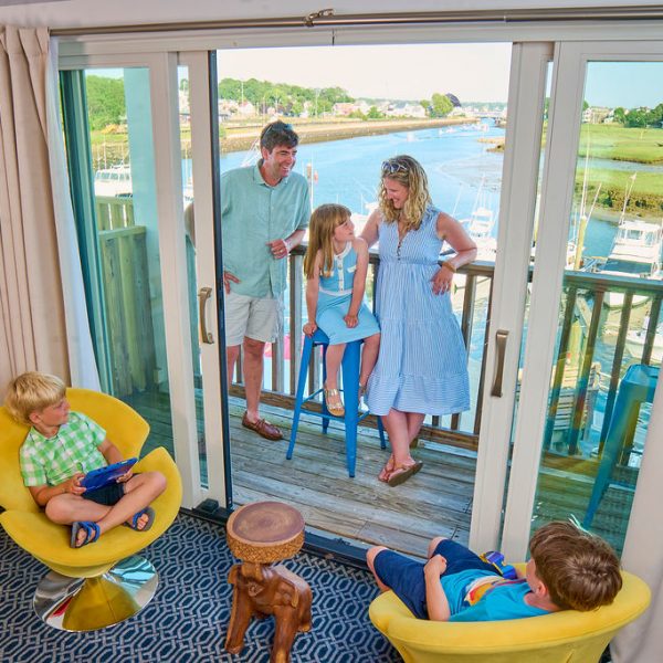 Parents and children in hotel suite overlooking water and marina. Three kids