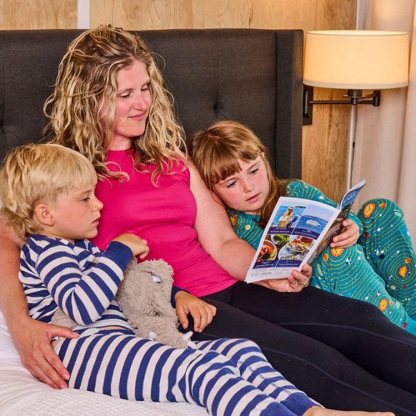 mom and two kids reading on hotel bed