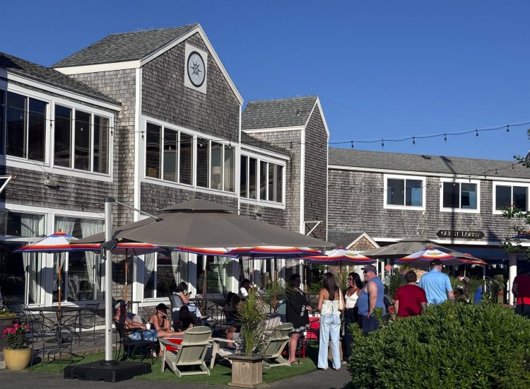 Outside a shingle 2 story builindg with umbrellas and people sitting