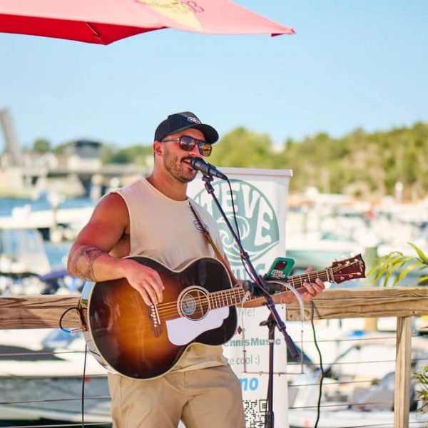 man playing guitar outside boats in the background sining