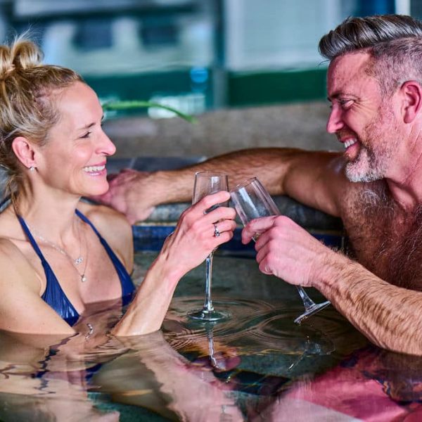 women and man in jacuzzi with champagne cheering