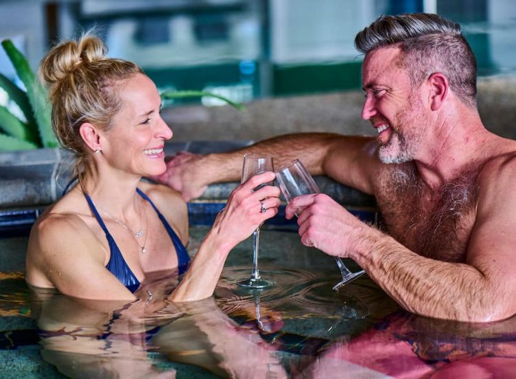 women and man in jacuzzi with champagne cheering
