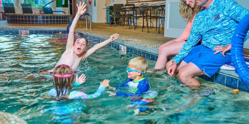Three kids in a pool with parents watching