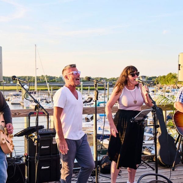 band playing on a deck with boats at a marina in the background