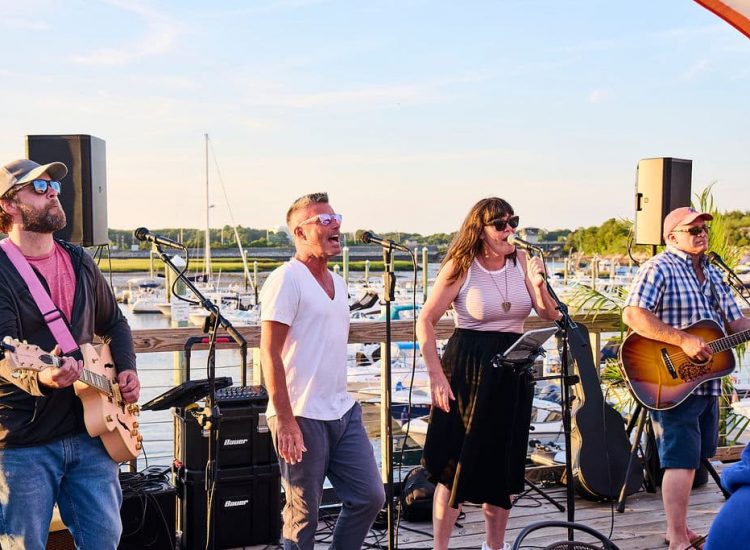 band playing on a deck with boats at a marina in the background