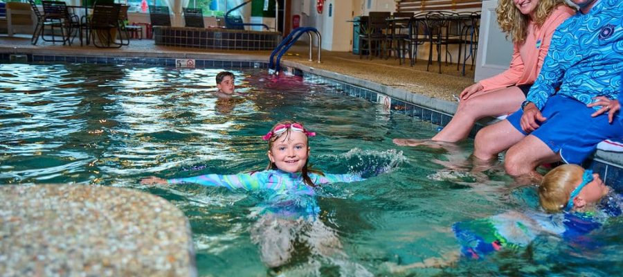 girl in swimshirt goggles on head in pool with parents watching
