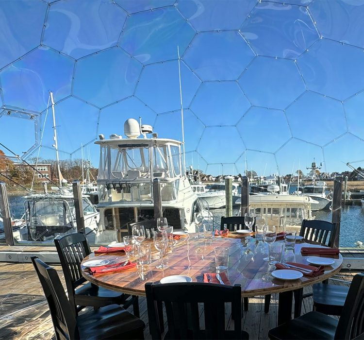 Clear dome dining table chairs daytime overlooking a marina and boats