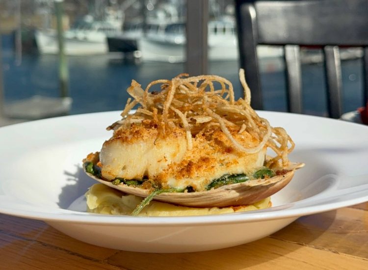 Scallop-rockafellar on a plate with water and boats in the background