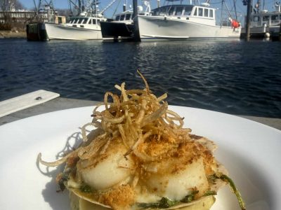 Scallop-rockafellar on a plate with water and boats in the background