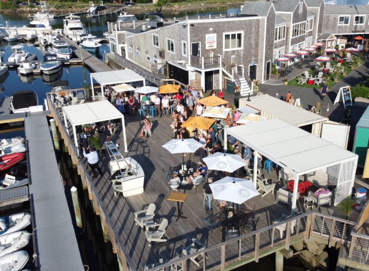 drone shot of Sun Deck cabanas and umbrellas with people on a d eck at a marina