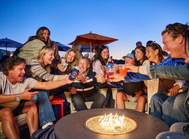 men and ladies cheers over a fire pit on a deck at sunset